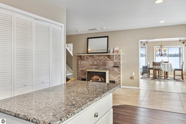 kitchen featuring dark stone countertops, a fireplace, white cabinetry, and a notable chandelier