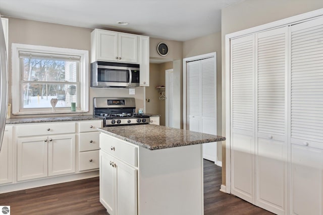 kitchen with dark wood-style floors, a kitchen island, dark stone countertops, stainless steel appliances, and white cabinetry