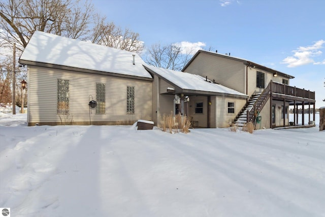 snow covered rear of property with stairway and a deck