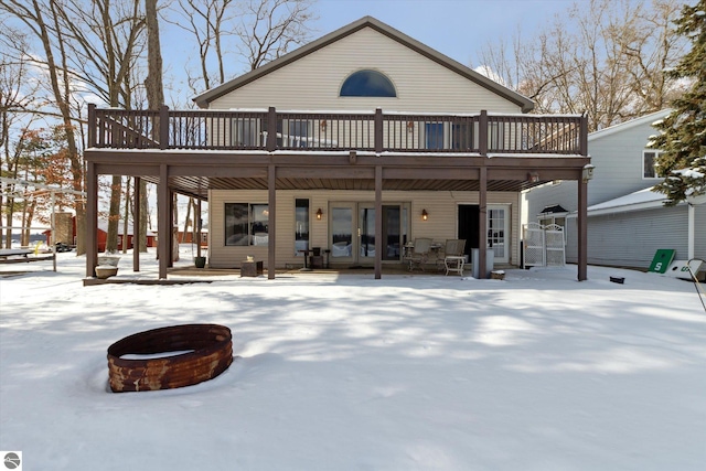 snow covered back of property with a fire pit, french doors, and a wooden deck