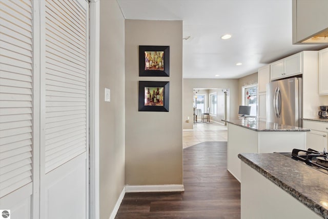 kitchen featuring baseboards, white cabinets, dark wood-style floors, dark stone countertops, and freestanding refrigerator