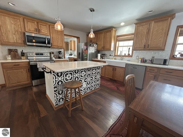 kitchen with stainless steel appliances, light countertops, hanging light fixtures, a kitchen island, and a sink