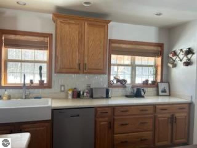 kitchen with dishwasher, light countertops, tasteful backsplash, and brown cabinets