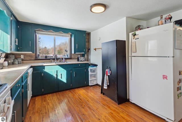 kitchen featuring white appliances, light wood finished floors, light countertops, blue cabinetry, and a sink