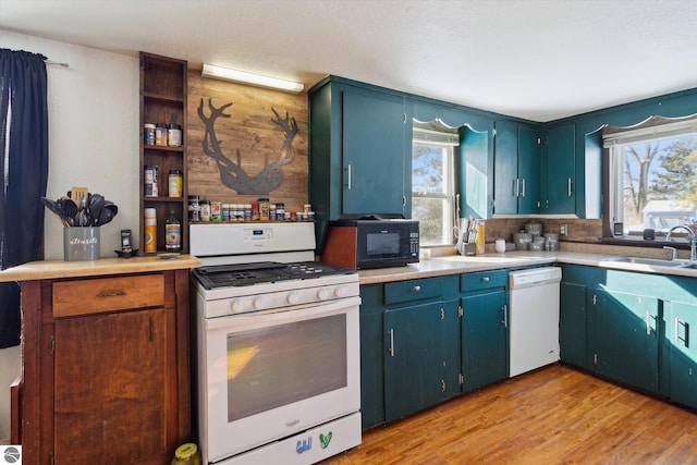 kitchen with light countertops, light wood-style flooring, a sink, a textured ceiling, and white appliances