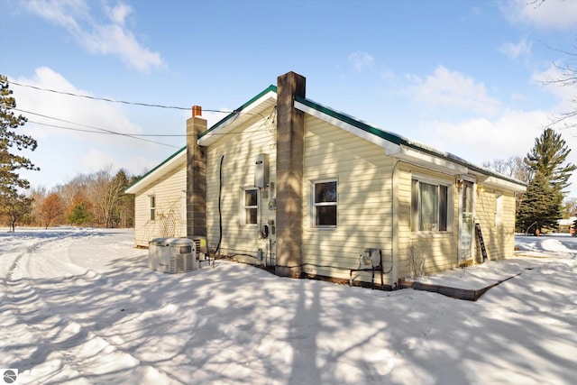 snow covered property featuring a chimney and central AC