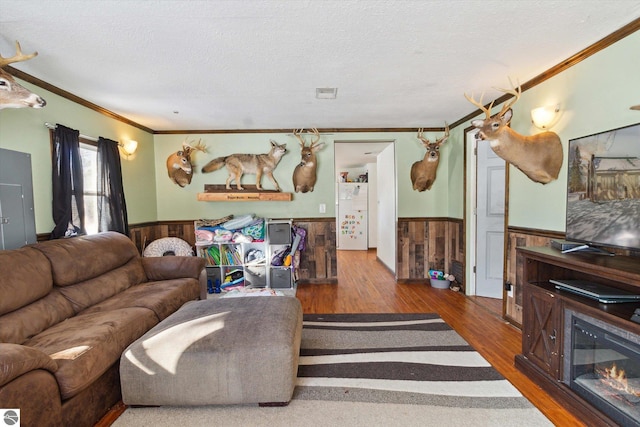 living room with ornamental molding, wainscoting, wooden walls, a textured ceiling, and wood finished floors