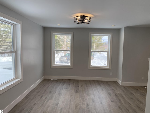 empty room with a wealth of natural light, light wood-style flooring, and baseboards