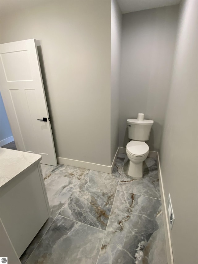 bathroom with toilet, marble finish floor, baseboards, and vanity