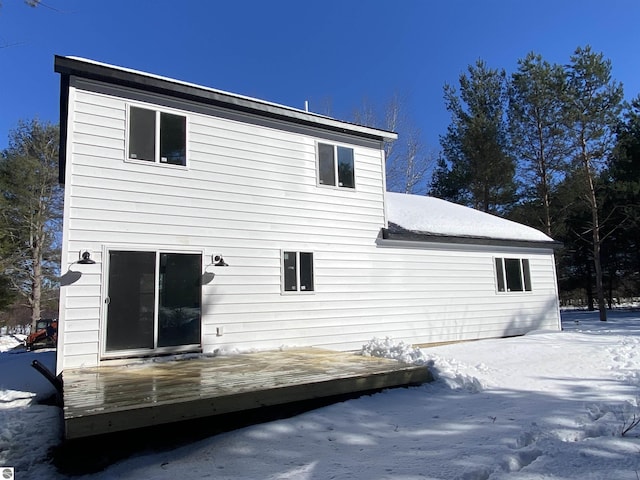 snow covered back of property with a wooden deck