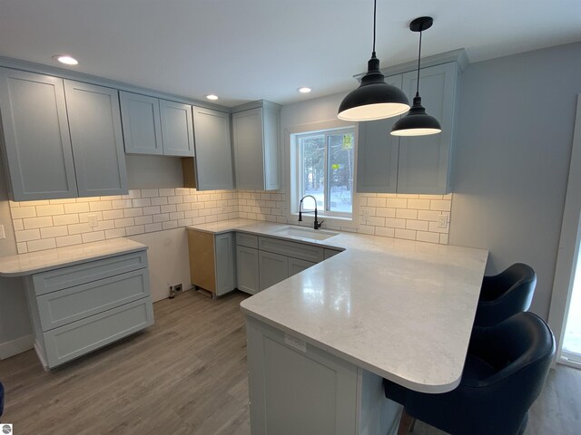 kitchen featuring a peninsula, a sink, light countertops, light wood-style floors, and backsplash