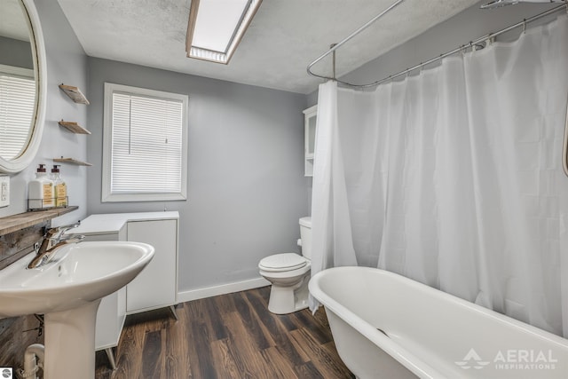 full bathroom featuring a bathtub, toilet, a healthy amount of sunlight, wood finished floors, and baseboards
