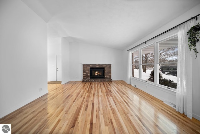 unfurnished living room with light wood finished floors, lofted ceiling, visible vents, a brick fireplace, and baseboards