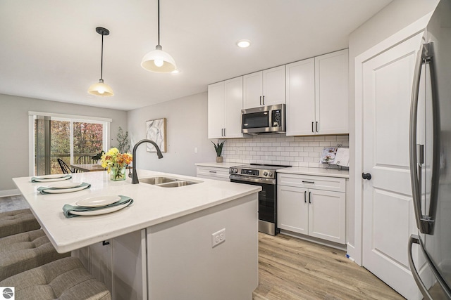 kitchen featuring a center island with sink, hanging light fixtures, appliances with stainless steel finishes, white cabinets, and a sink