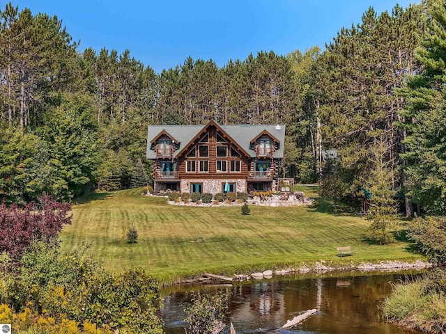 back of house featuring a water view, stone siding, a forest view, and a lawn