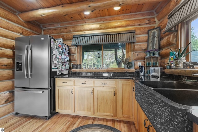 kitchen featuring beam ceiling, stainless steel refrigerator with ice dispenser, light wood finished floors, light brown cabinetry, and dark stone countertops