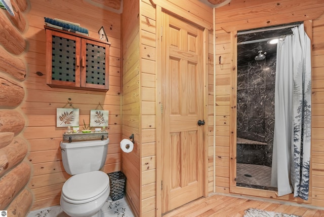 bathroom featuring a stall shower, wooden walls, toilet, and wood finished floors