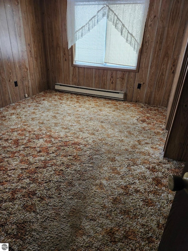 unfurnished room with a baseboard heating unit, carpet floors, and wooden walls