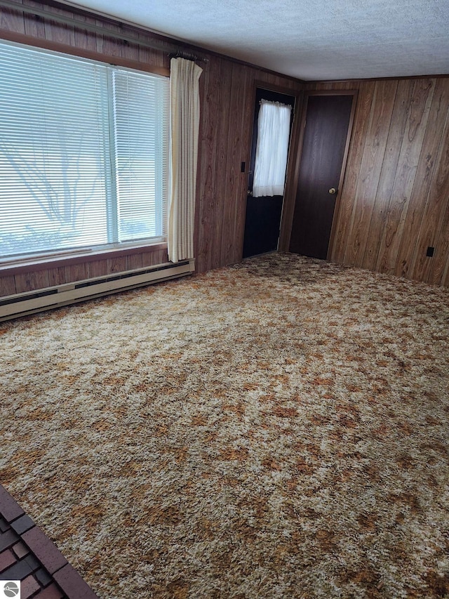 carpeted spare room with a baseboard heating unit, wooden walls, and a textured ceiling