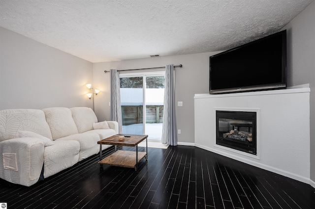 living area with a textured ceiling, visible vents, dark wood-style flooring, and a glass covered fireplace