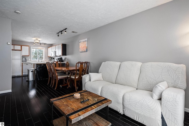 living area with baseboards, visible vents, dark wood-type flooring, rail lighting, and a textured ceiling