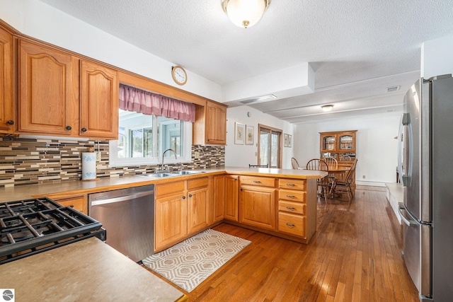 kitchen with decorative backsplash, appliances with stainless steel finishes, a sink, light wood-type flooring, and a peninsula