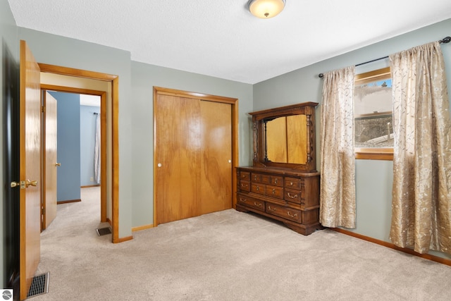 bedroom with light carpet, baseboards, visible vents, a textured ceiling, and a closet