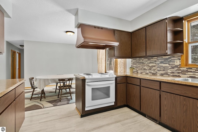 kitchen with white electric stove, light countertops, decorative backsplash, and range hood