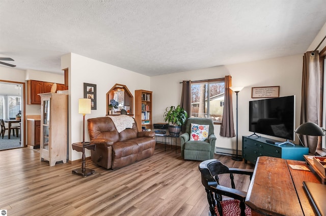 living room featuring ceiling fan, light wood-style flooring, baseboard heating, and a textured ceiling