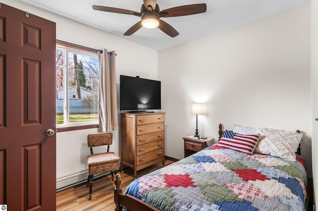 bedroom with light wood-style flooring, a baseboard heating unit, and ceiling fan