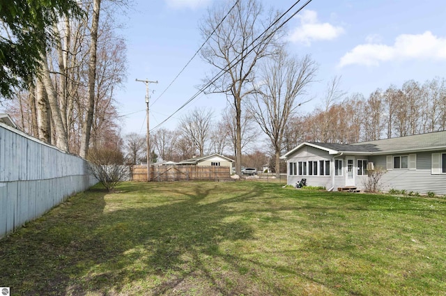 view of yard featuring entry steps, a sunroom, and a fenced backyard