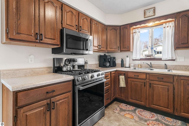 kitchen featuring brown cabinetry, stainless steel appliances, a sink, and light countertops