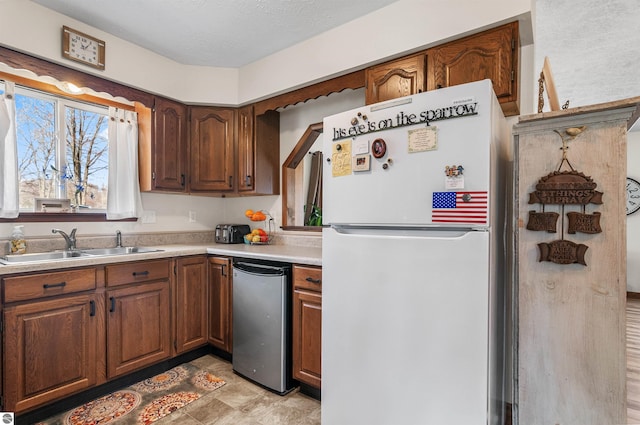 kitchen with brown cabinets, light countertops, freestanding refrigerator, a sink, and a textured ceiling