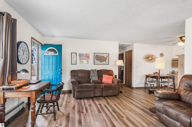 living room with a textured ceiling, light wood finished floors, baseboard heating, and a wall unit AC