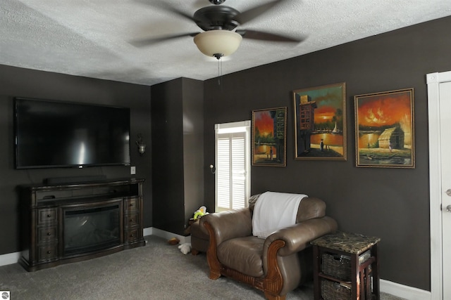 living area featuring carpet, a glass covered fireplace, ceiling fan, a textured ceiling, and baseboards