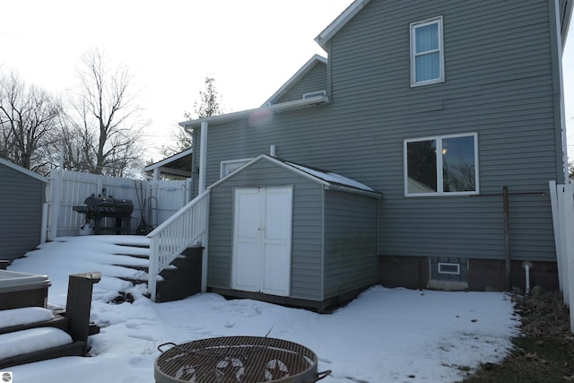 snow covered property with an outbuilding, fence, a fire pit, and a shed