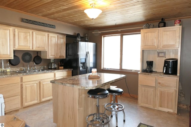 kitchen with stainless steel fridge, a center island, light countertops, light brown cabinetry, and a sink