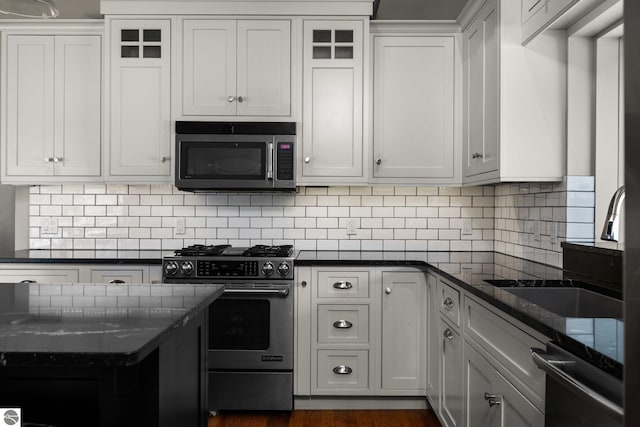 kitchen with white cabinetry, a sink, stainless steel gas range oven, and dark stone countertops