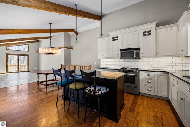 kitchen featuring dark countertops, appliances with stainless steel finishes, glass insert cabinets, hanging light fixtures, and white cabinetry