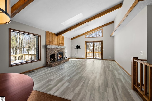 living area with high vaulted ceiling, a fireplace, a skylight, light wood-type flooring, and beamed ceiling