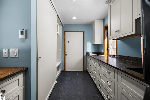 kitchen featuring dark countertops, white cabinets, a textured ceiling, dark tile patterned floors, and baseboards