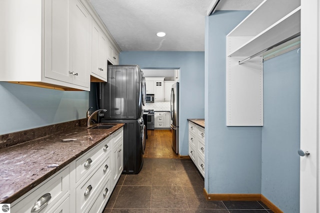 kitchen with decorative backsplash, appliances with stainless steel finishes, white cabinets, a sink, and dark stone counters