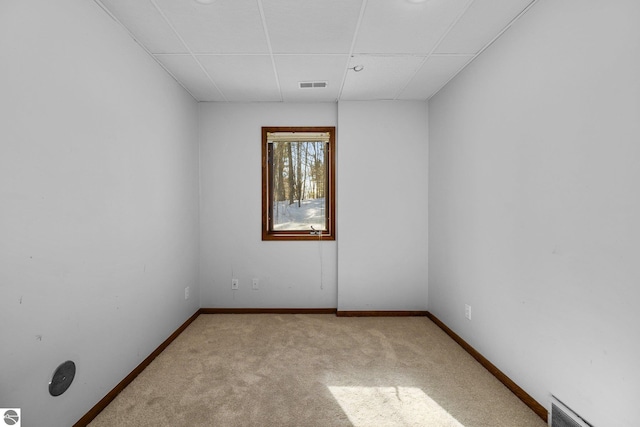 carpeted spare room featuring a paneled ceiling, visible vents, and baseboards