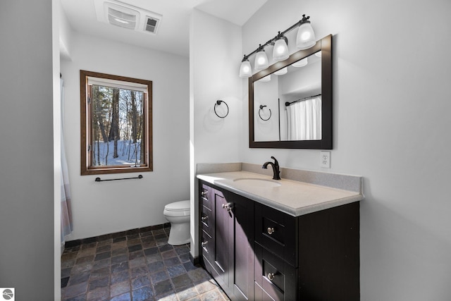 bathroom featuring stone finish flooring, visible vents, vanity, and toilet