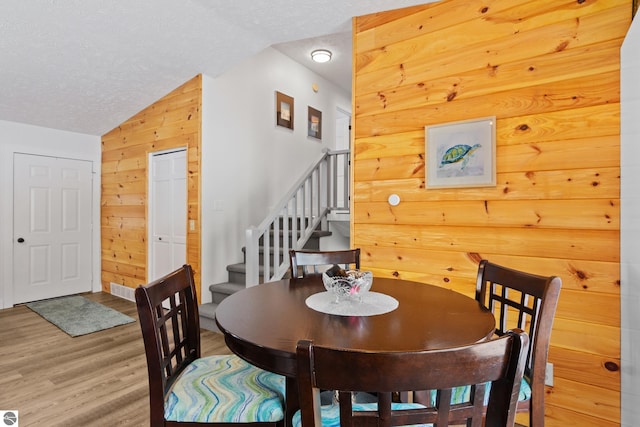 dining room featuring a textured ceiling, lofted ceiling, wood walls, wood finished floors, and stairs