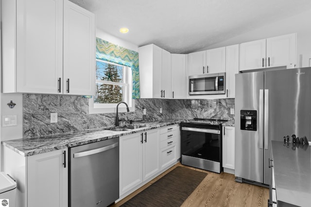 kitchen featuring stainless steel appliances, a sink, white cabinetry, backsplash, and light stone countertops