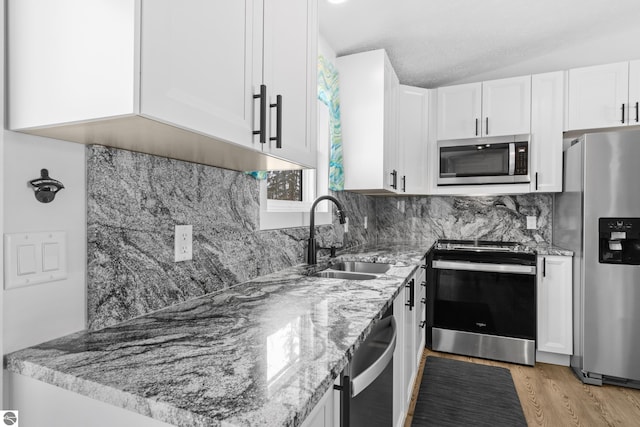 kitchen with stainless steel appliances, white cabinetry, vaulted ceiling, a sink, and light stone countertops