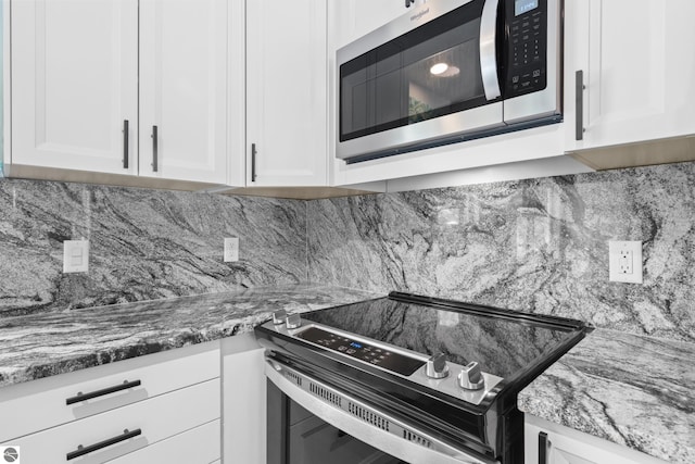 kitchen featuring stainless steel appliances, white cabinetry, backsplash, and dark stone countertops