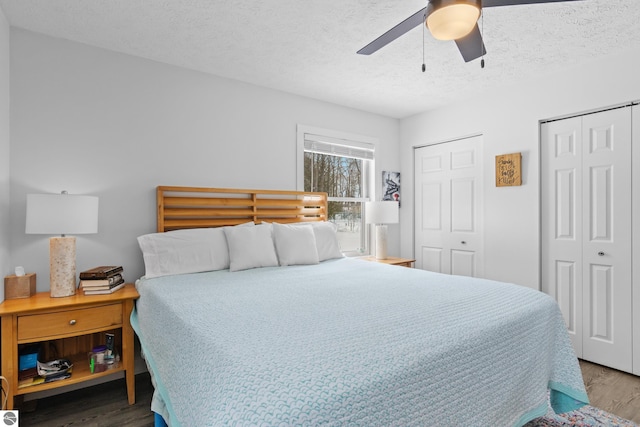 bedroom with a textured ceiling, ceiling fan, wood finished floors, and two closets