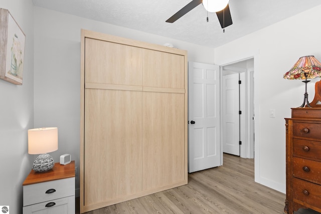 bedroom featuring a textured ceiling, a ceiling fan, baseboards, a closet, and light wood-type flooring